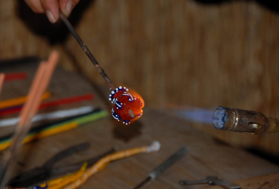 Eine gelbe Perle mit blau-weiß-roten Schichtaugen und kleinen Widderköpfen als Verzierung, gelbes Glas verfärbt sich während der Bearbeitung
